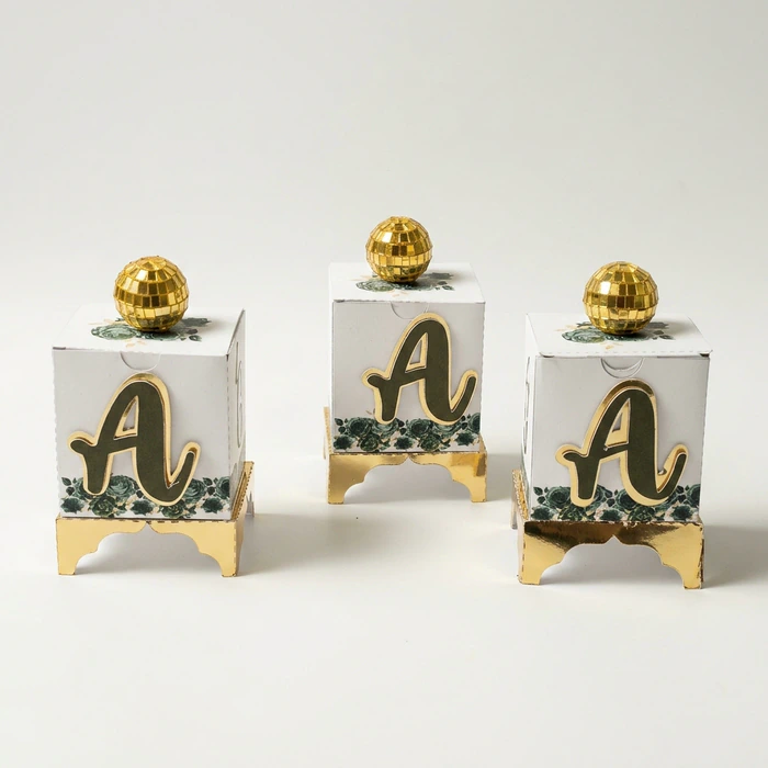 Three monogrammed favour boxes with gold bases, photographed in the studio