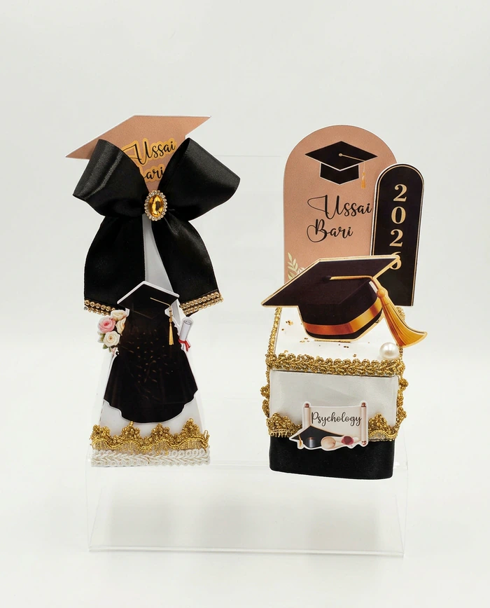 Two graduation keepsakes with a miniature gown, a gold tasselled cap and personalised name cards