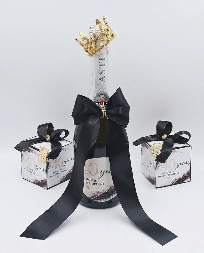 A decorated sparkling wine bottle with a gold crown, a wide black satin bow and two matching favour boxes